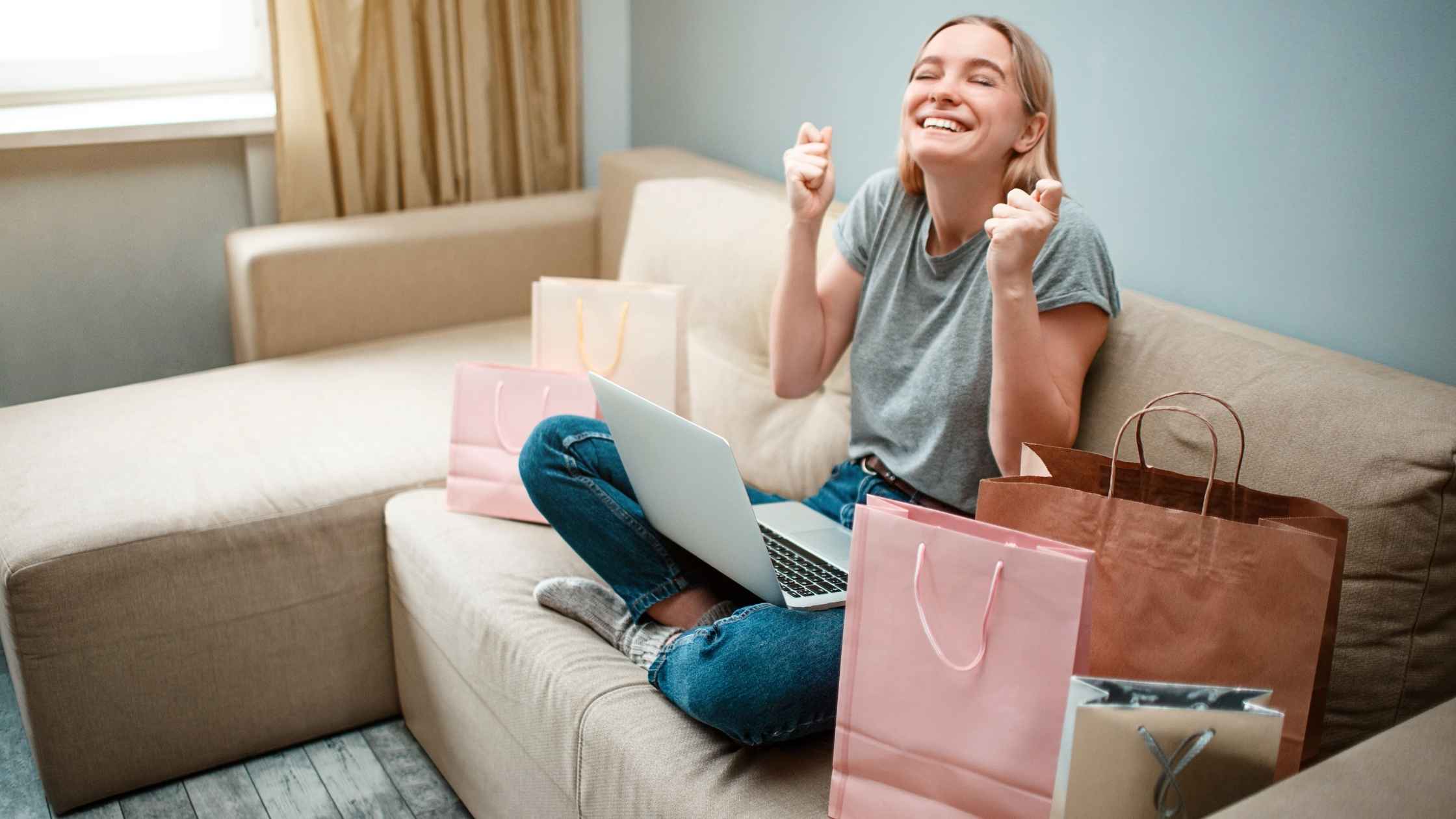 Happy woman using laptop at home surrounded by shopping bags, showing how to earn legit money online.