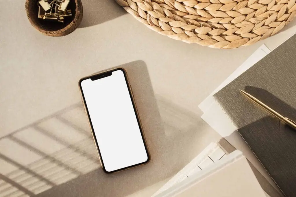 Flat lay of a smartphone on a desk with a notepad and accessories, representing how to earn money from playing games on your phone.