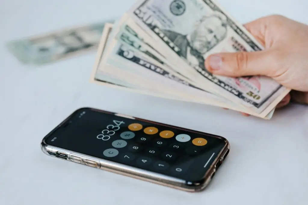 Mobile phone showing a calculator app near a person holding a pile of cash, representing making money online.