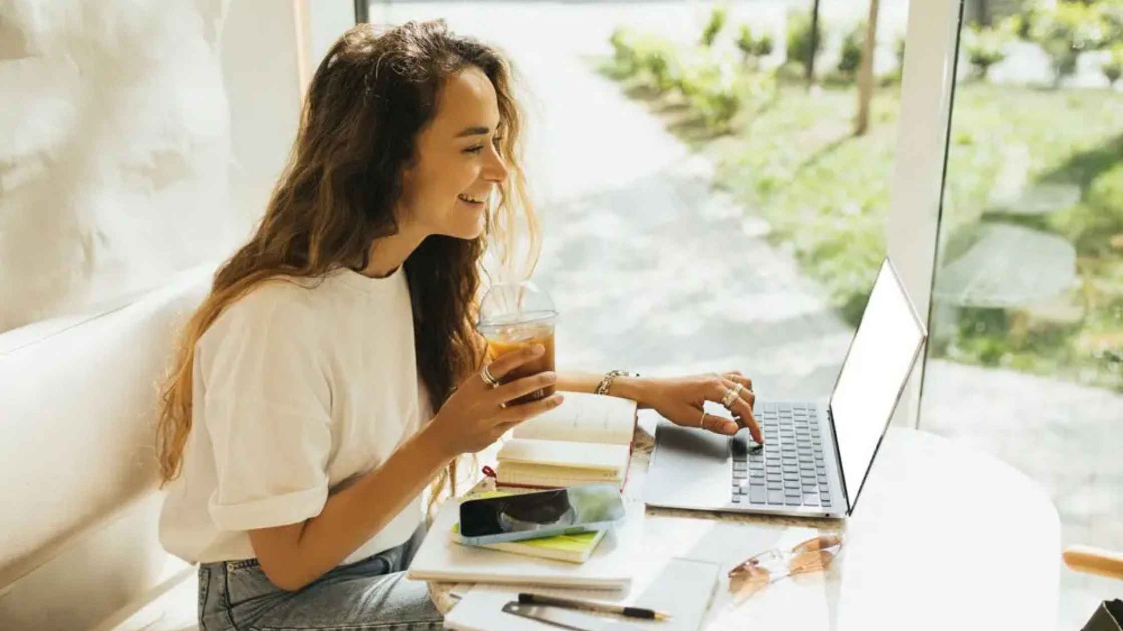 Freelancer working on a laptop with a drink in hand, planning how to turn freelance work into a business.