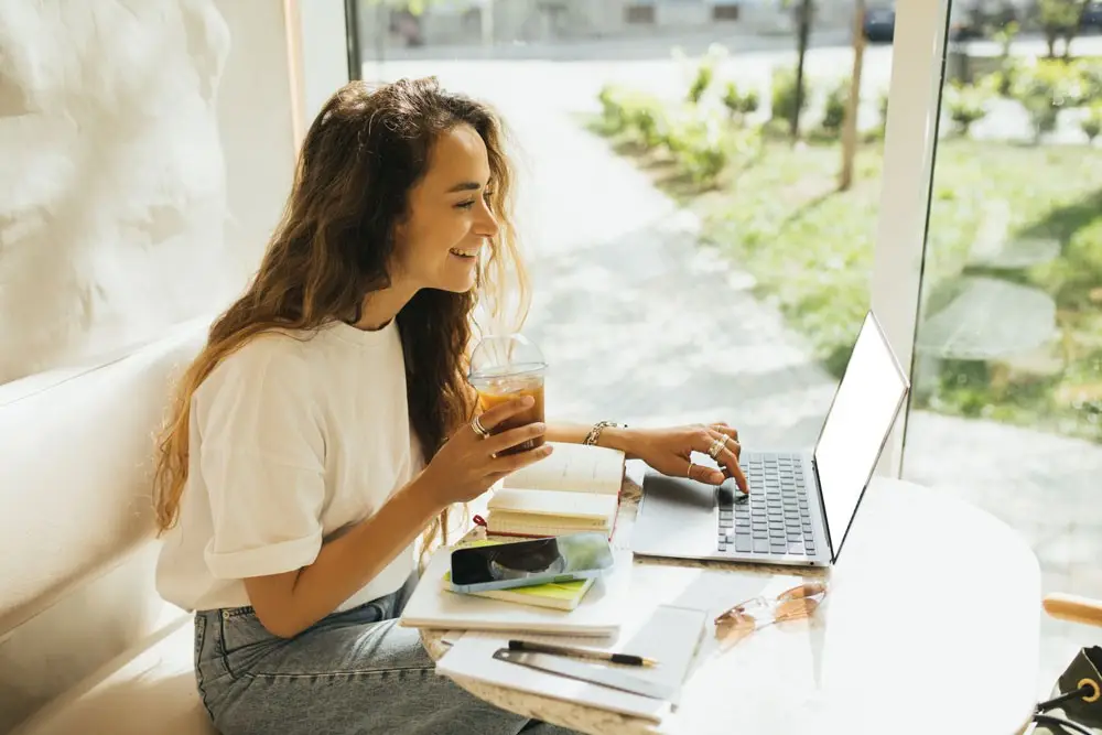 Freelancer working on a laptop with a drink in hand, planning how to turn freelance work into a business.