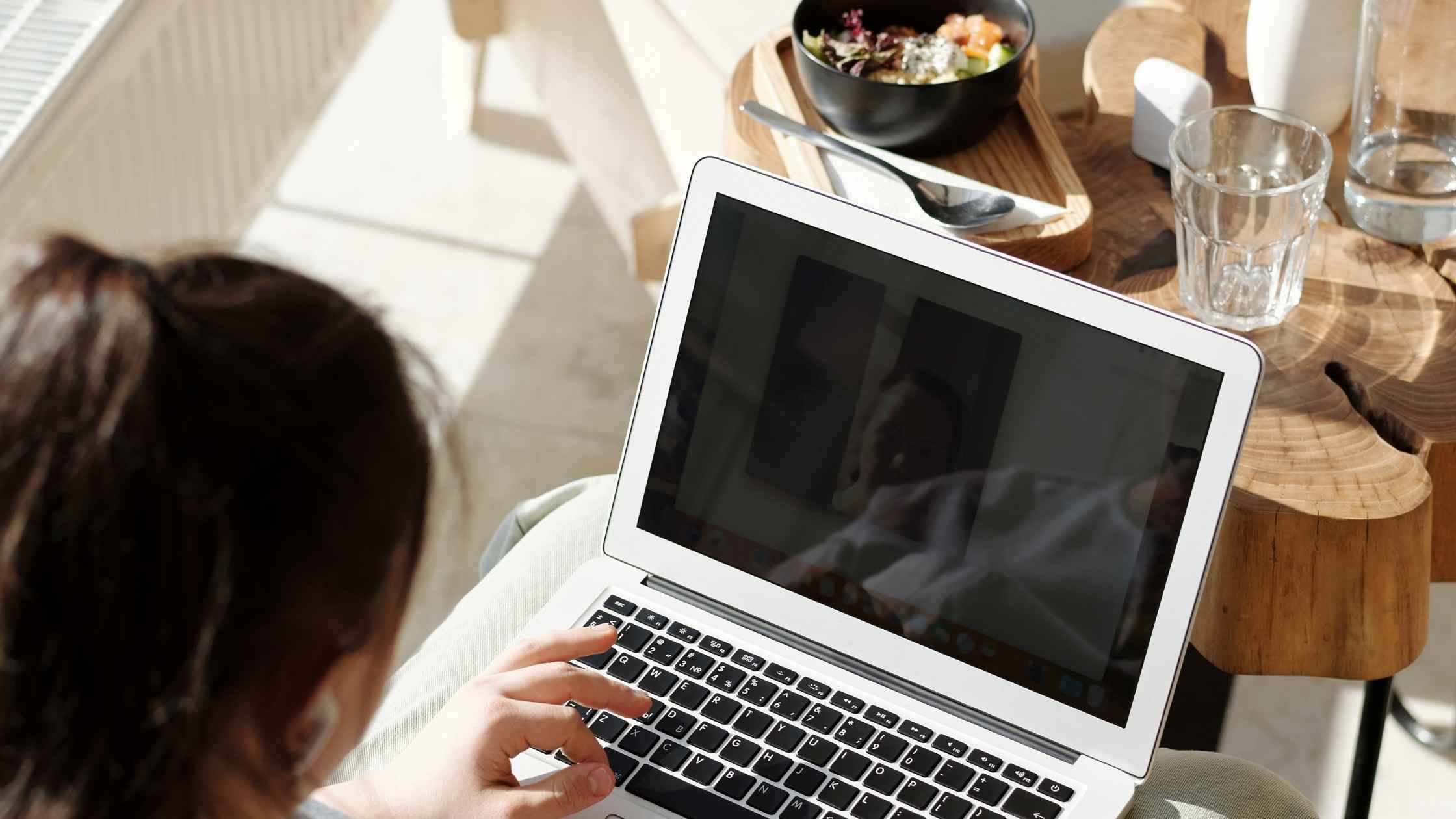 A person working on a laptop with a bowl of salad and glass of water nearby, representing remote work opportunities.