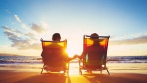 Two people sitting on beach chairs watching the sunset over the ocean, symbolizing a peaceful and stress-free retirement.