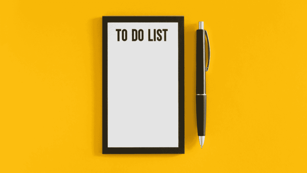 To-do list pad and pen on a vibrant yellow background, representing productivity and organization while working from home.