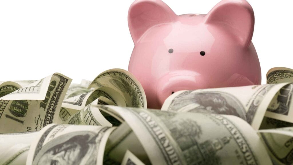 A pink piggy bank surrounded by bundles of US dollar bills, representing earnings through apps to win real money.