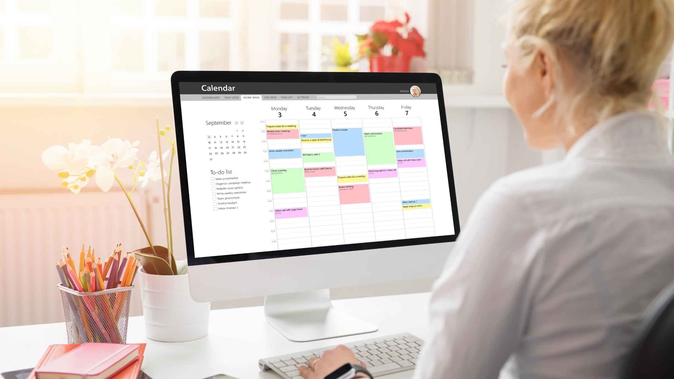 Woman using a digital planner on her computer screen to organize her workweek, showcasing the benefits of a digital planner side hustle.