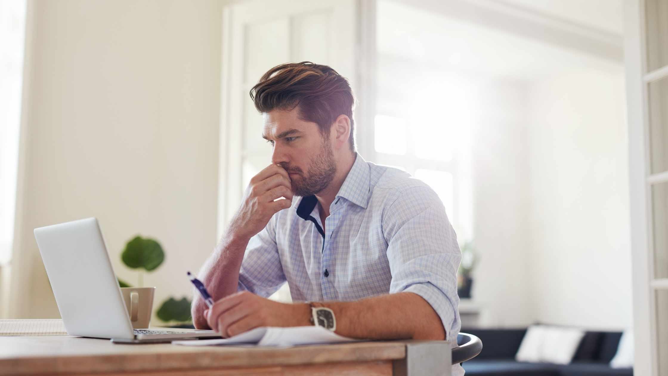 A focused man working remotely from home, exploring entry-level remote jobs on his laptop.