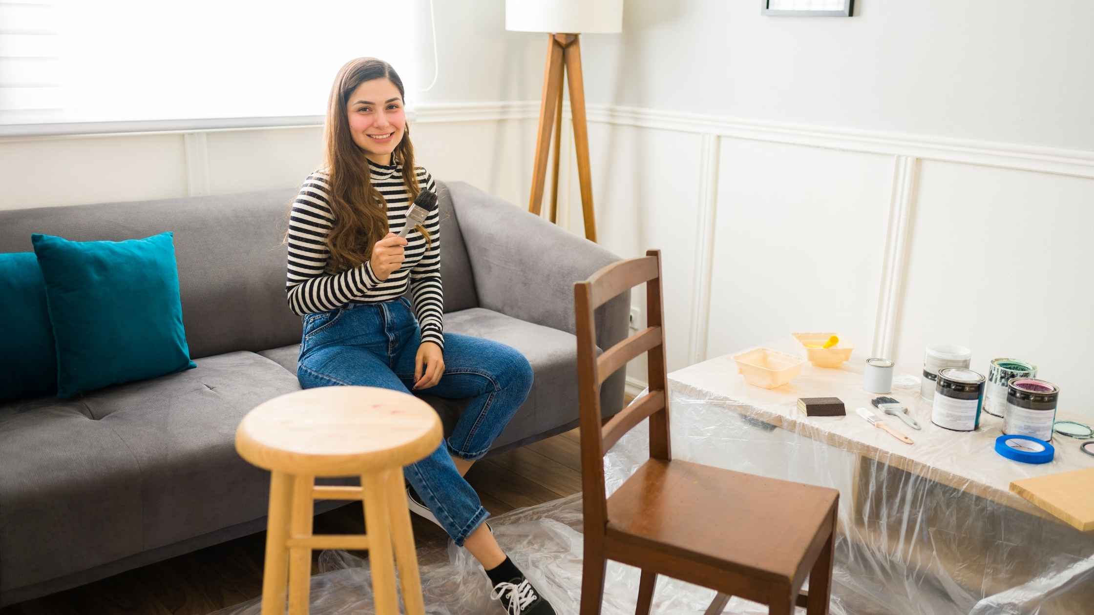 Woman working on her flipping furniture side hustle, preparing to refurbish a wooden chair with paint and tools.