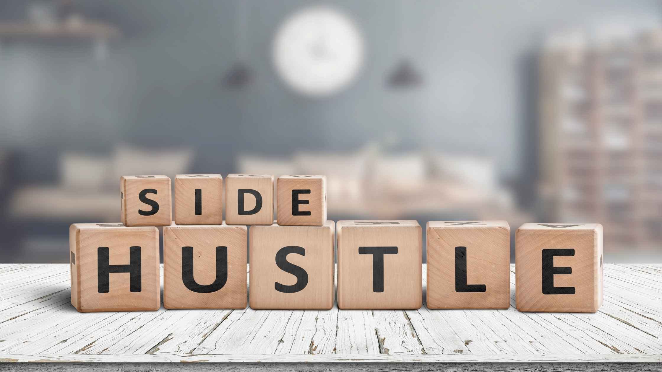 Wooden blocks spelling "Side Hustle" on a white wooden surface, representing fun side hustles and creative ways to earn extra income.