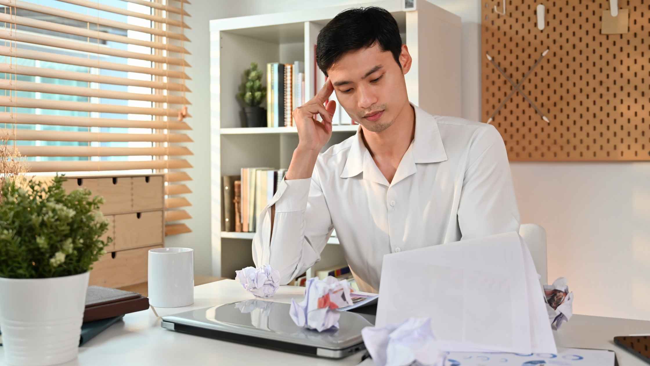 A frustrated blogger sitting at a desk with crumpled papers, struggling with common blogging mistakes to avoid.