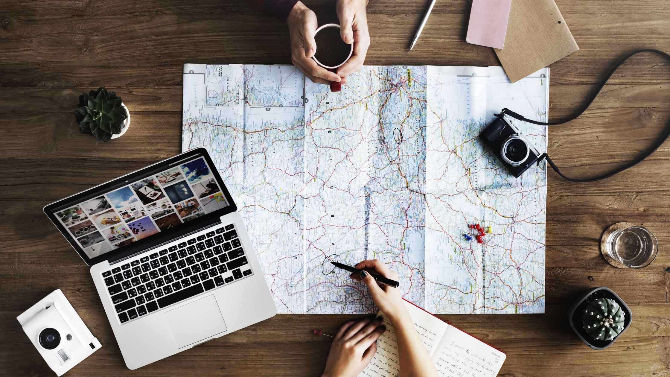 Planning a business purchase with a map, laptop, and camera on a wooden table.