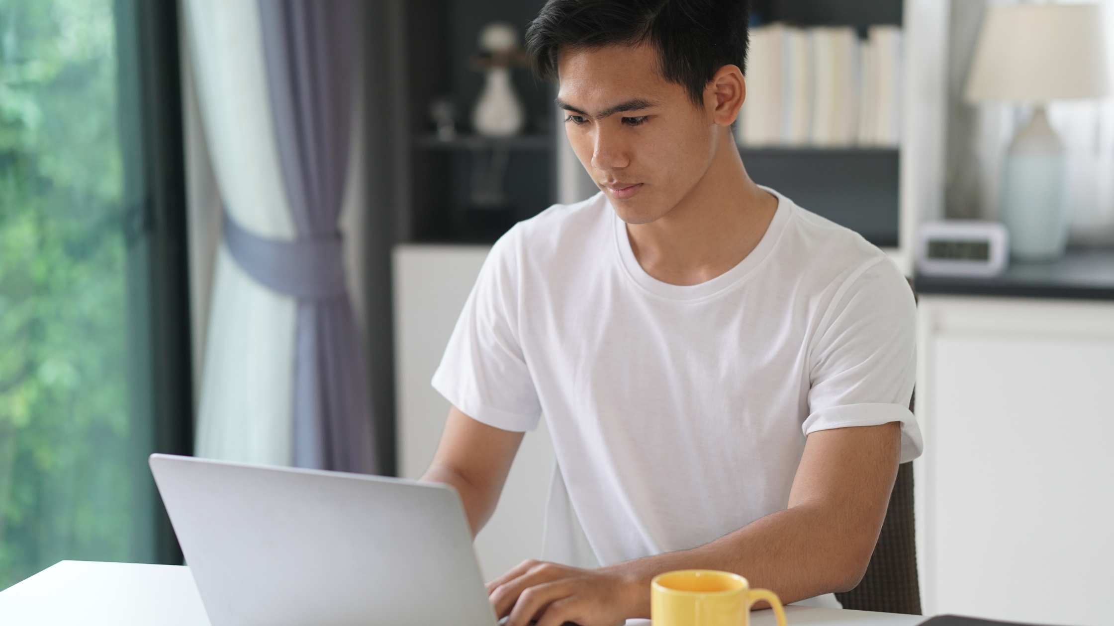 Young man working on a laptop at home, focused on building a side hustle