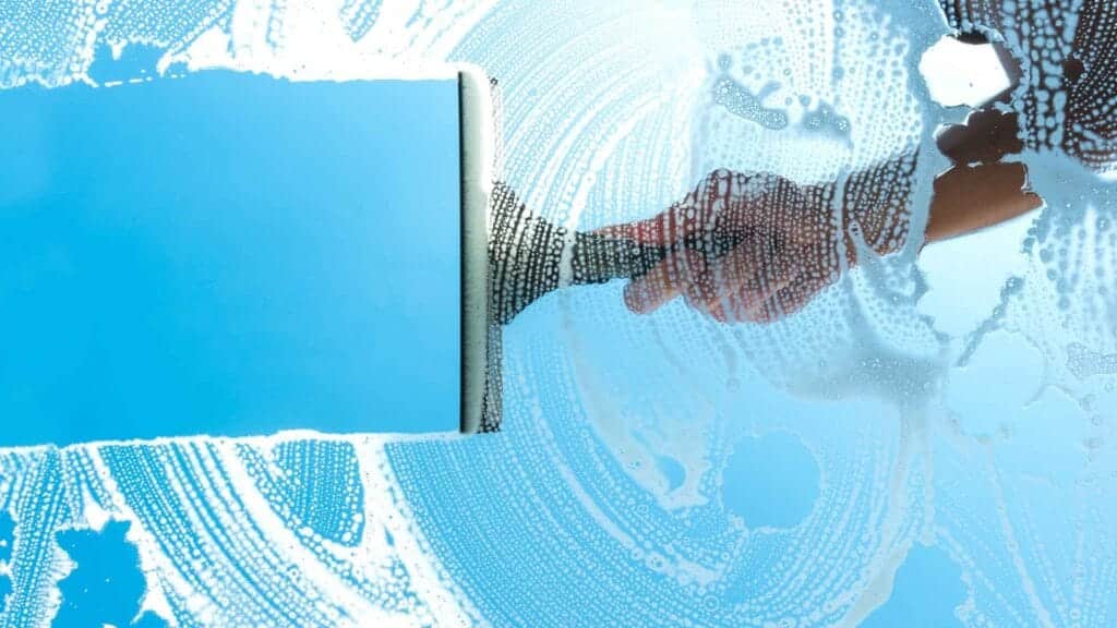 A hand using a squeegee to clean a window, representing a successful window cleaning side hustle.