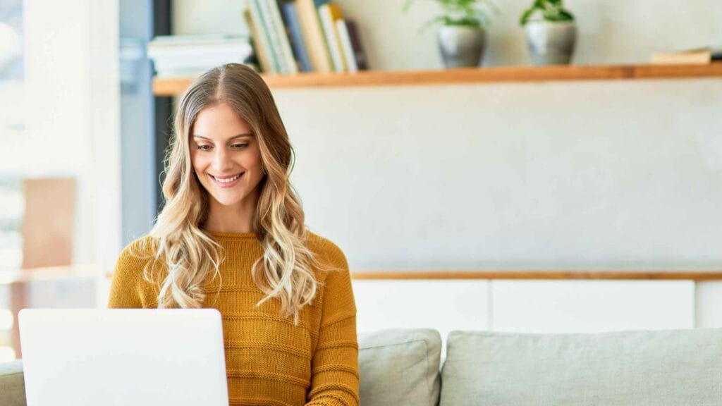 A smiling woman working on her laptop in a cozy home setting, representing a beginner setting up my first blog.