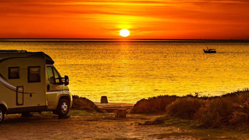 Small camper parked by the ocean at sunset, symbolizing freedom and budget-friendly DIY small camper interior ideas