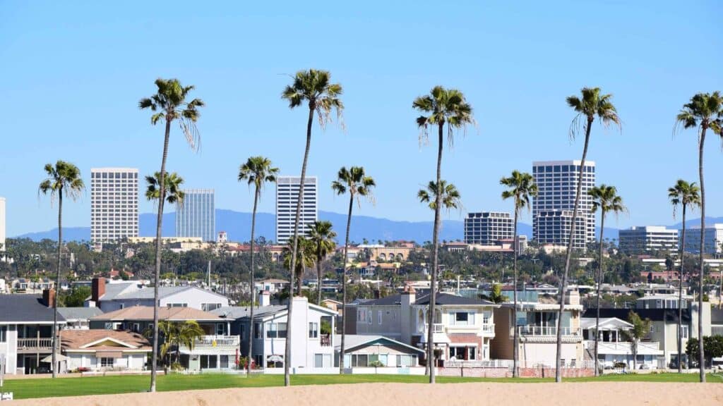 View of California coastal homes and high-rise buildings with palm trees under a clear sky.