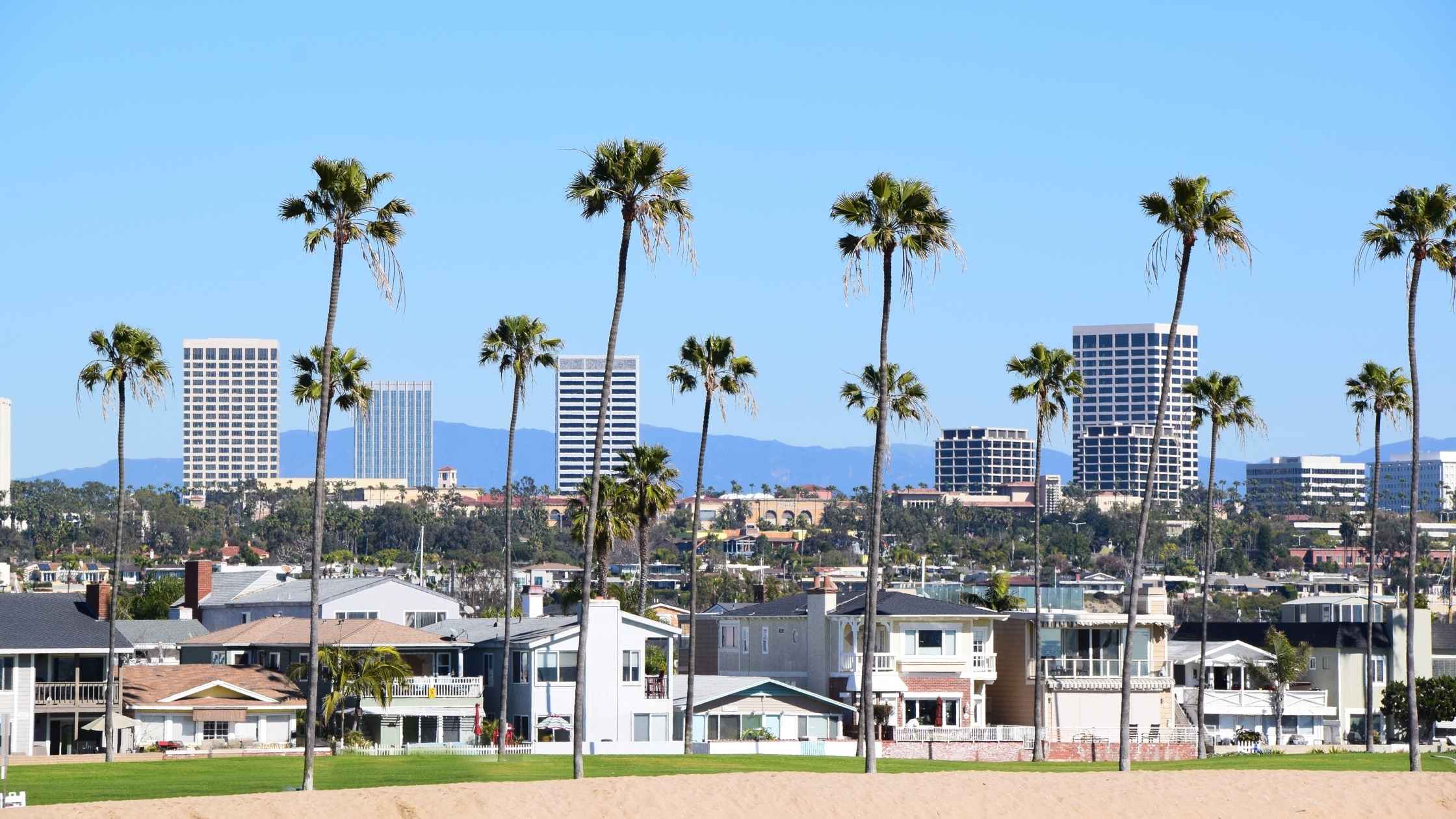 View of California coastal homes and high-rise buildings with palm trees under a clear sky.