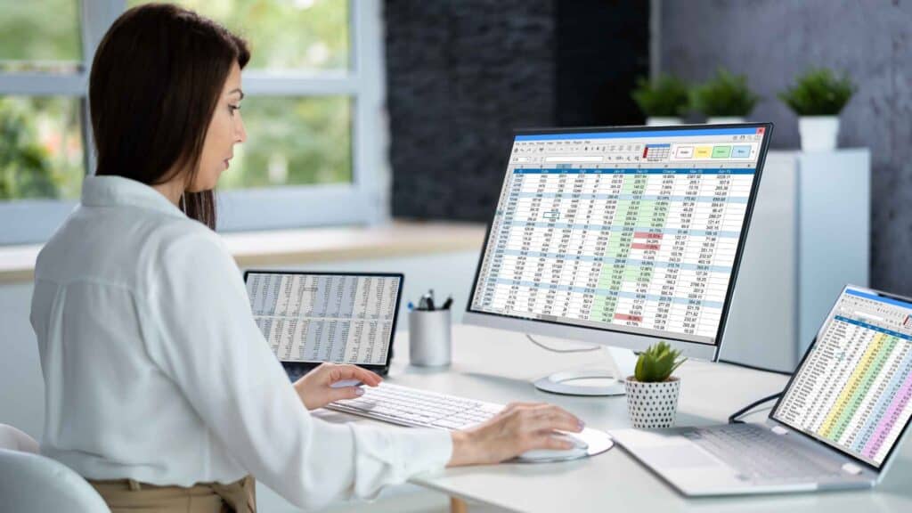 Woman reviewing a monthly expenses spreadsheet on multiple computer screens