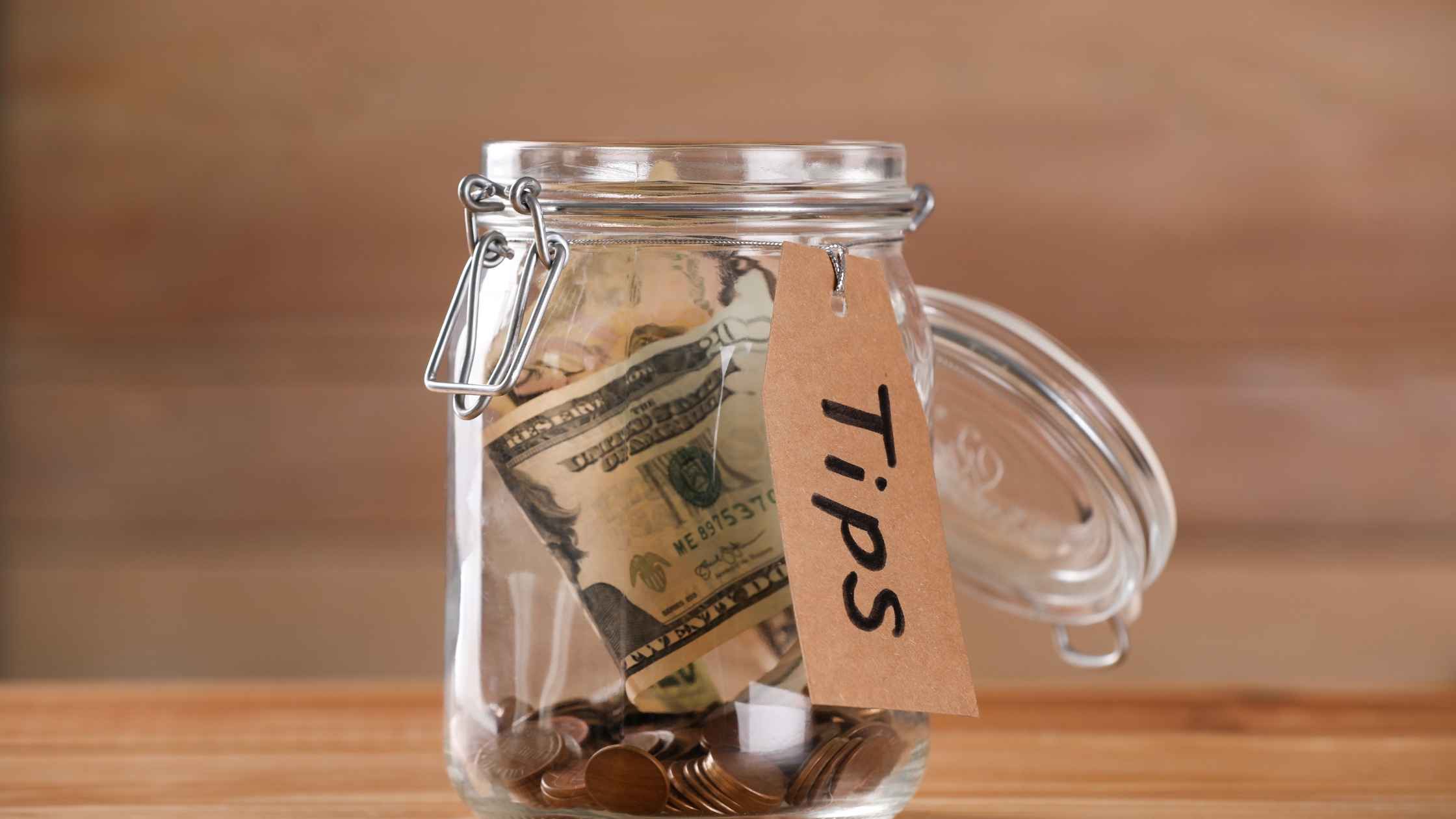 Glass jar labeled “Tips” filled with cash and coins, representing budgeting tips and money-saving strategies