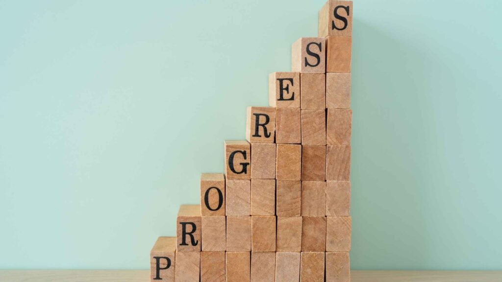 A stack of blocks that gets higher with each column representing how consistency builds progress, which leads to success.