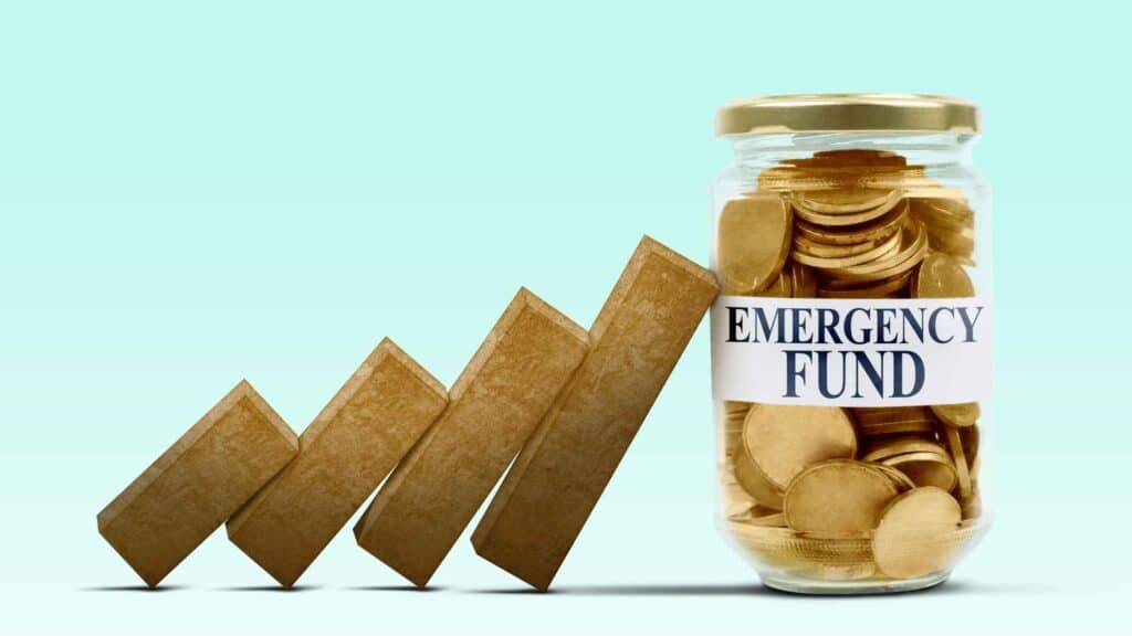 A bunch of weights leaning on a jar filled with money that says "Emergency Fund" on the outside, representing an emergency fund that supports unforeseen time of finance needs.