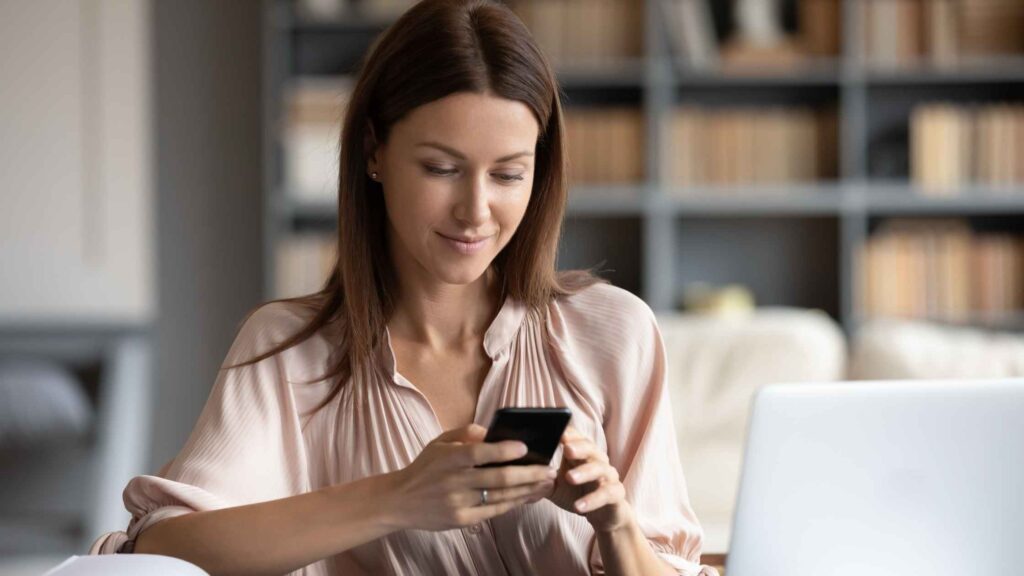 A woman using her phone and laptop to read a blog post, which represents building a successful niche audience for blog monetization.