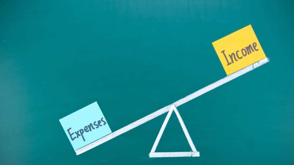 A scale that shows expenses outweighing income on one side, which represents a financial situation that calls for a solution to decrease expenses so that savings can be increased.