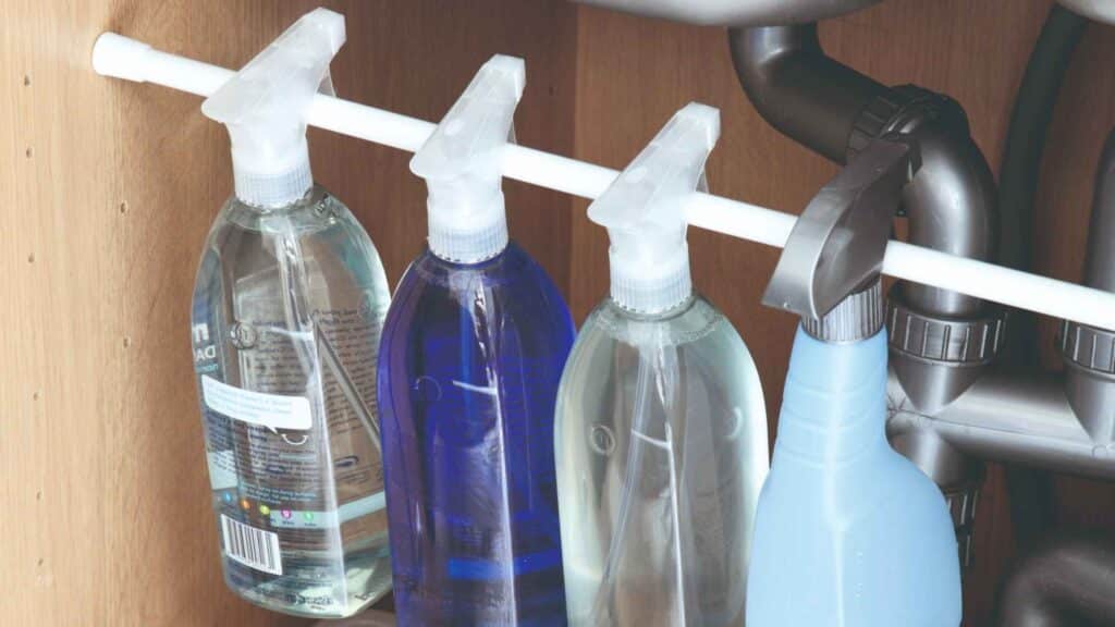 A tension rod under kitchen sink cabinets to hold spray bottles, emphasizing the difference diy small kitchen ideas can have on a kitchen