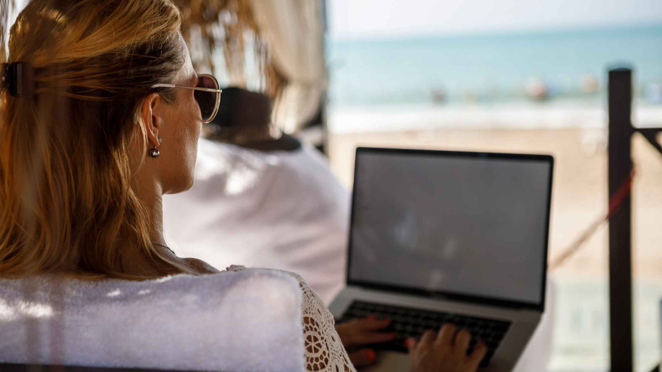 Woman sitting on the beach working on a laptop while brainstorming blog post ideas
