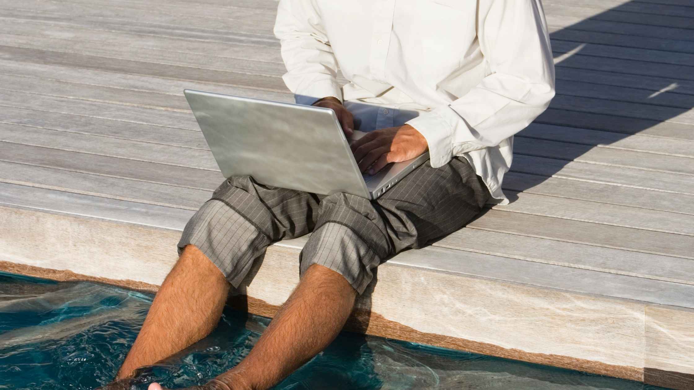 Man working on laptop by the pool while buying a business remotely