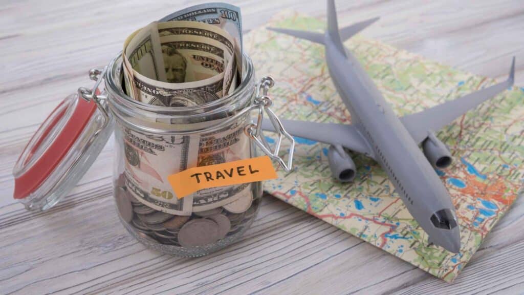 A map with a plane over it and a jar next to it that says "travel" filled with money. This represents budgeting and saving money to plan for travel expenses.